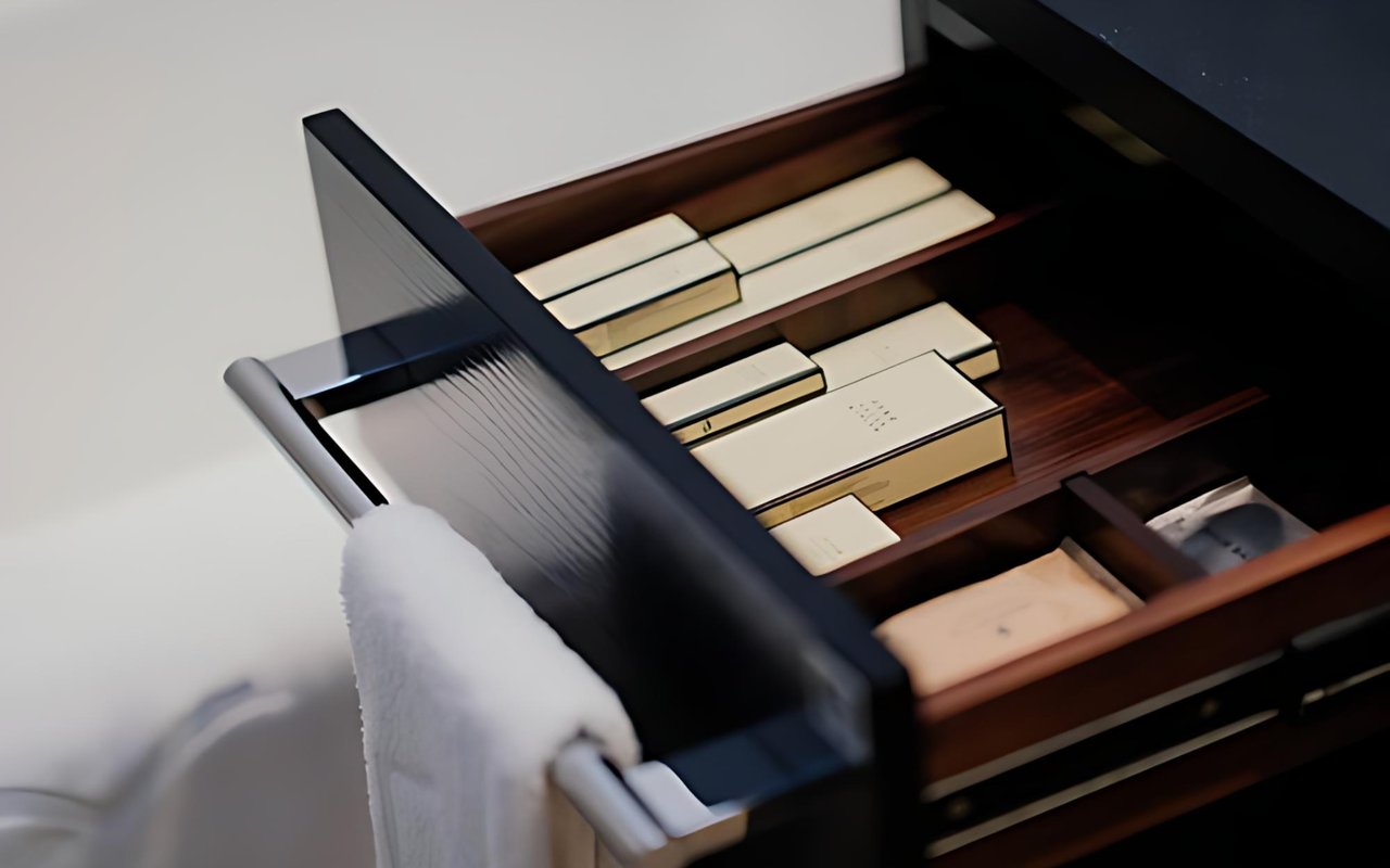 Open dark wooden drawer holding stationery, with a white towel draped over its handle.