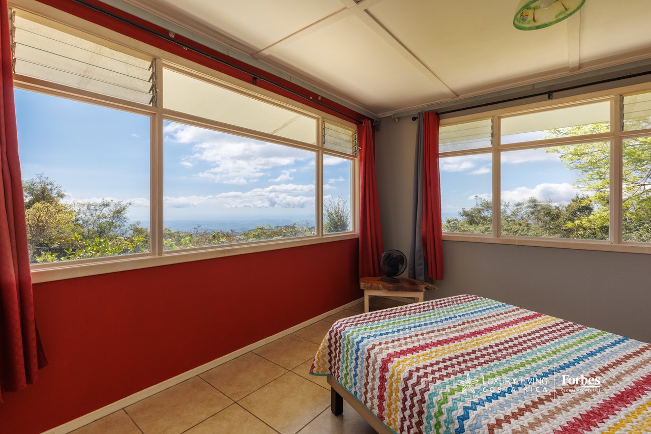Bedroom with red walls and wide windows overlooking green hills and a distant blue horizon.