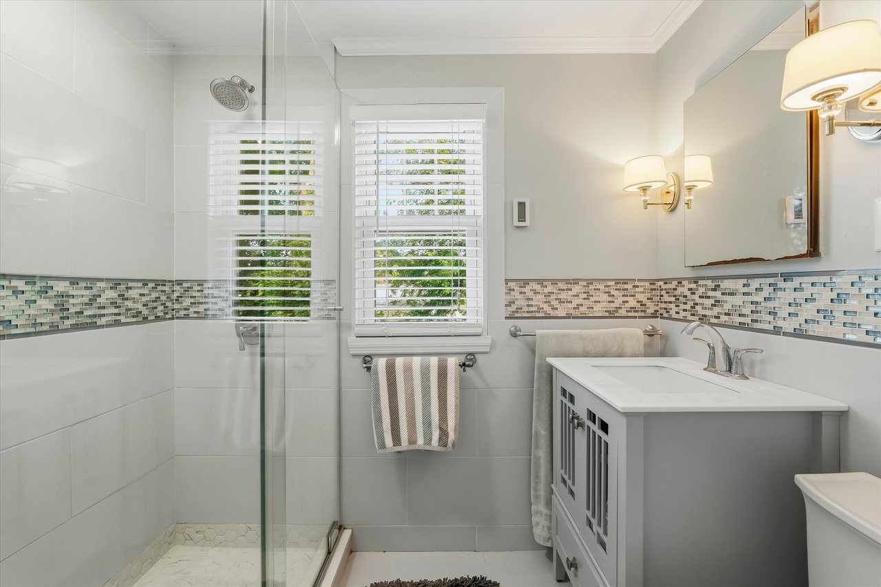 Bathroom with a glass walk-in shower, mosaic tile accent band, and white vanity.