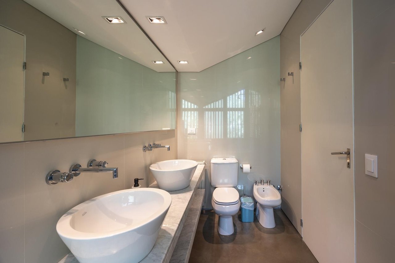 Modern bathroom with double vessel sinks, a long stone vanity, and toilet beside a bidet.