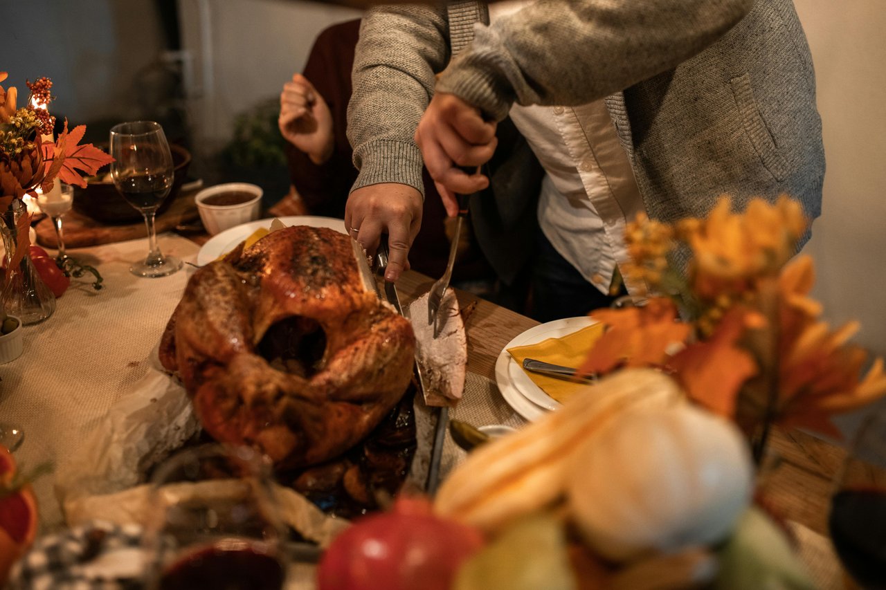 A person carving a roasted Thanksgiving turkey at a decorated fall table, capturing the warm holiday atmosphere featured in San Fernando Valley Thanksgiving events.