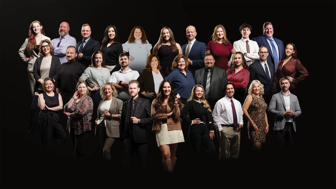 Real estate team posing together in several rows against a black background.