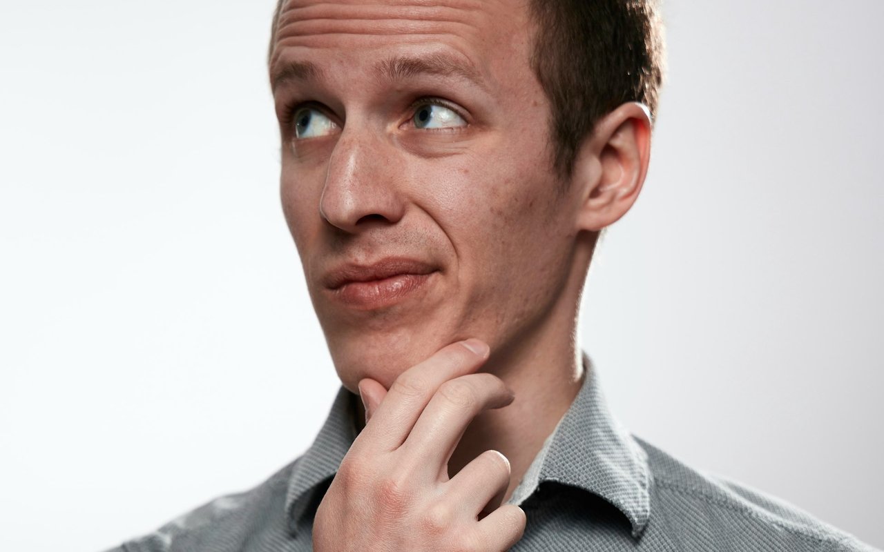 A man looks upward thoughtfully with his hand under his chin.