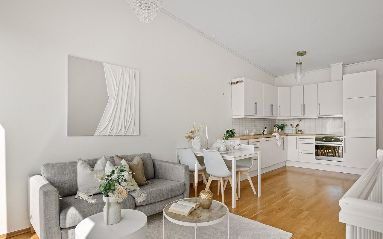Open-plan living room and kitchen with a gray sofa, white cabinets, and hardwood floors.