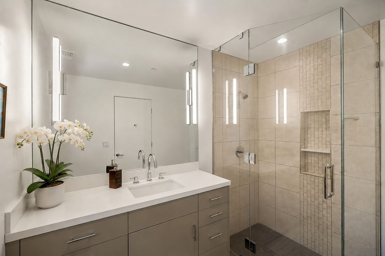 Contemporary bathroom with a white vanity, glass-enclosed tiled shower, and potted orchid.