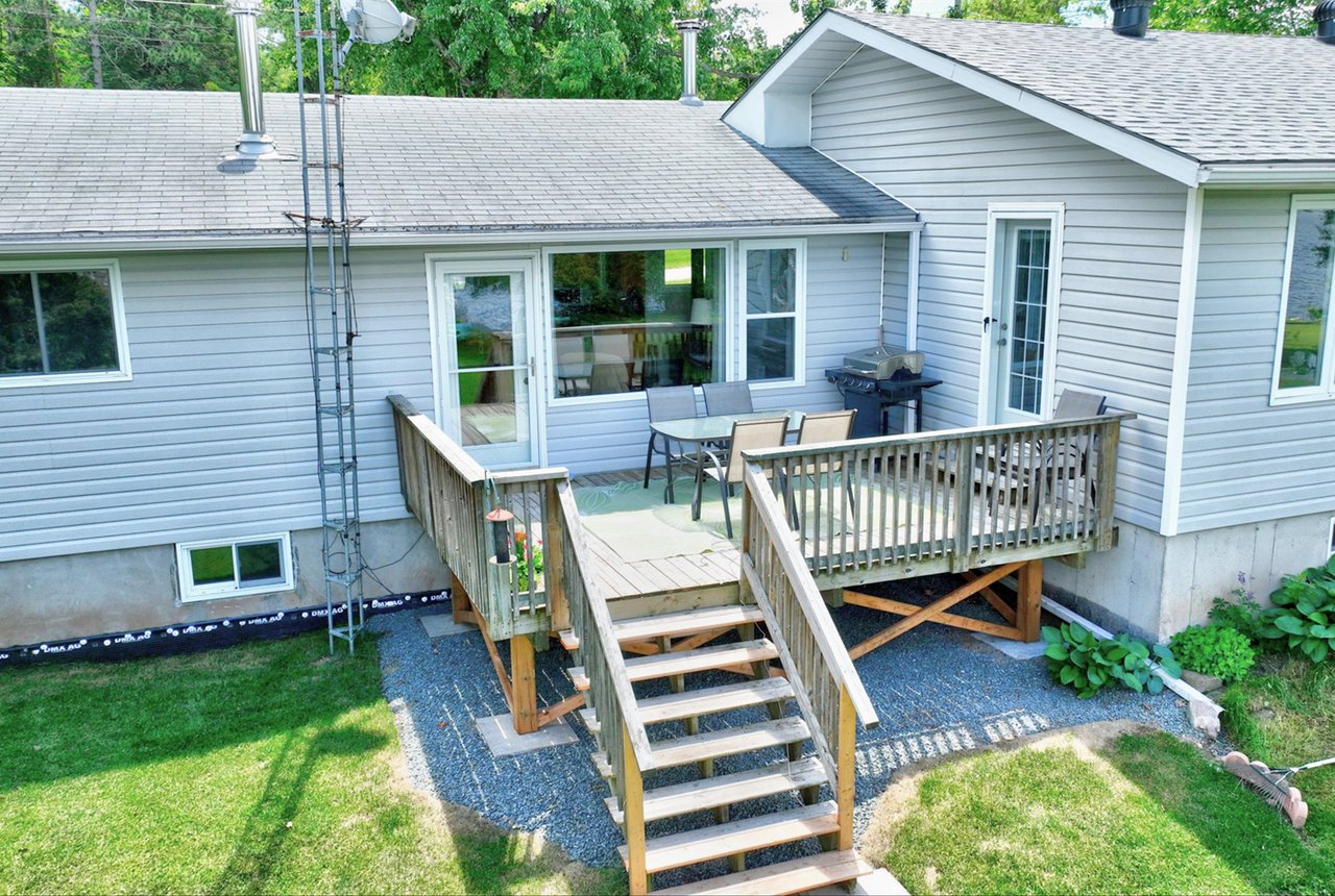Raised wooden deck with stairs, outdoor dining set, and barbecue beside a light-gray house.