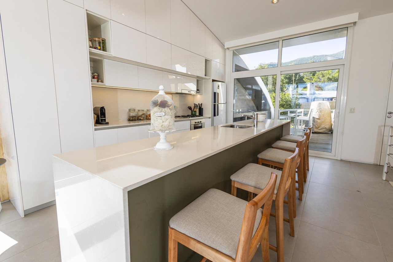 Modern kitchen with a long island and bar stools beside glass doors opening onto a patio.