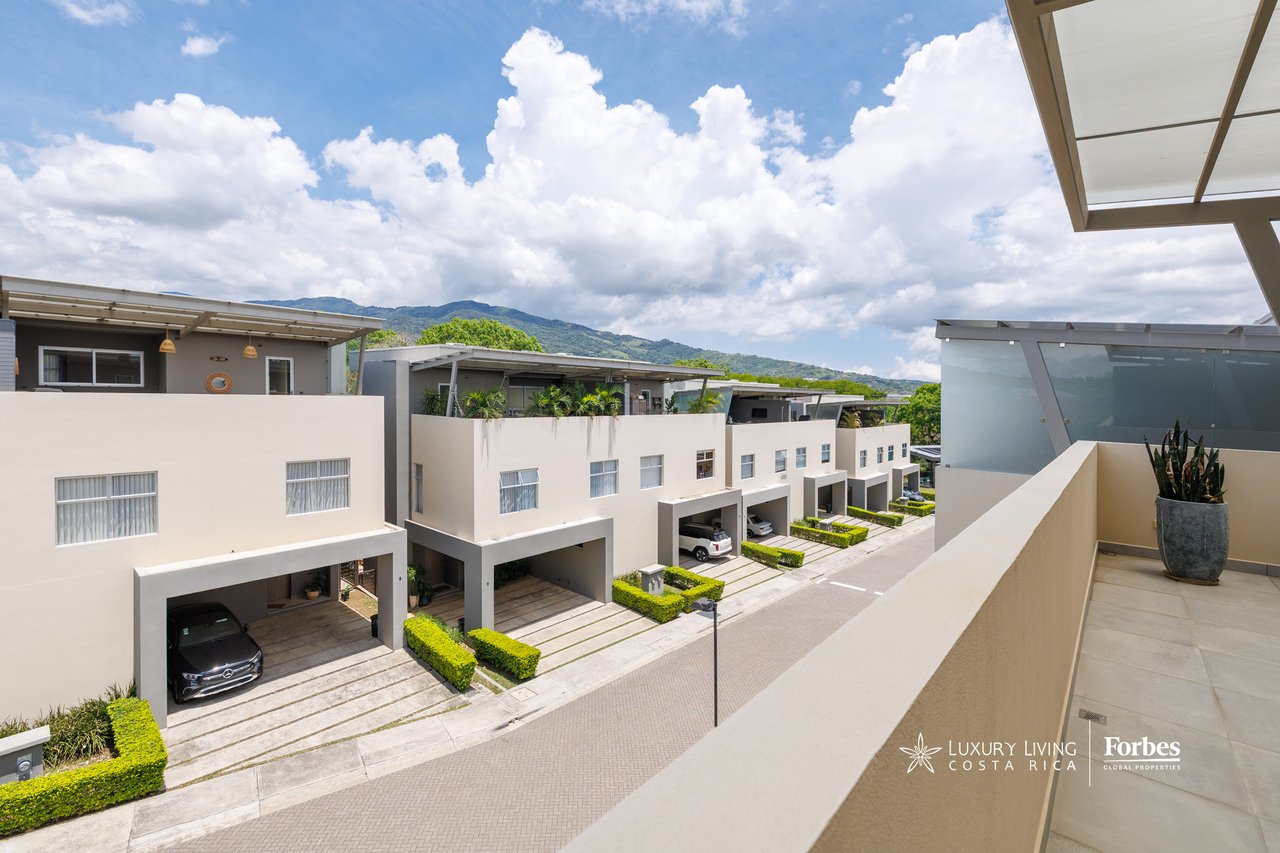 Modern white townhouses with rooftop terraces and landscaped carports, backed by green mountains.