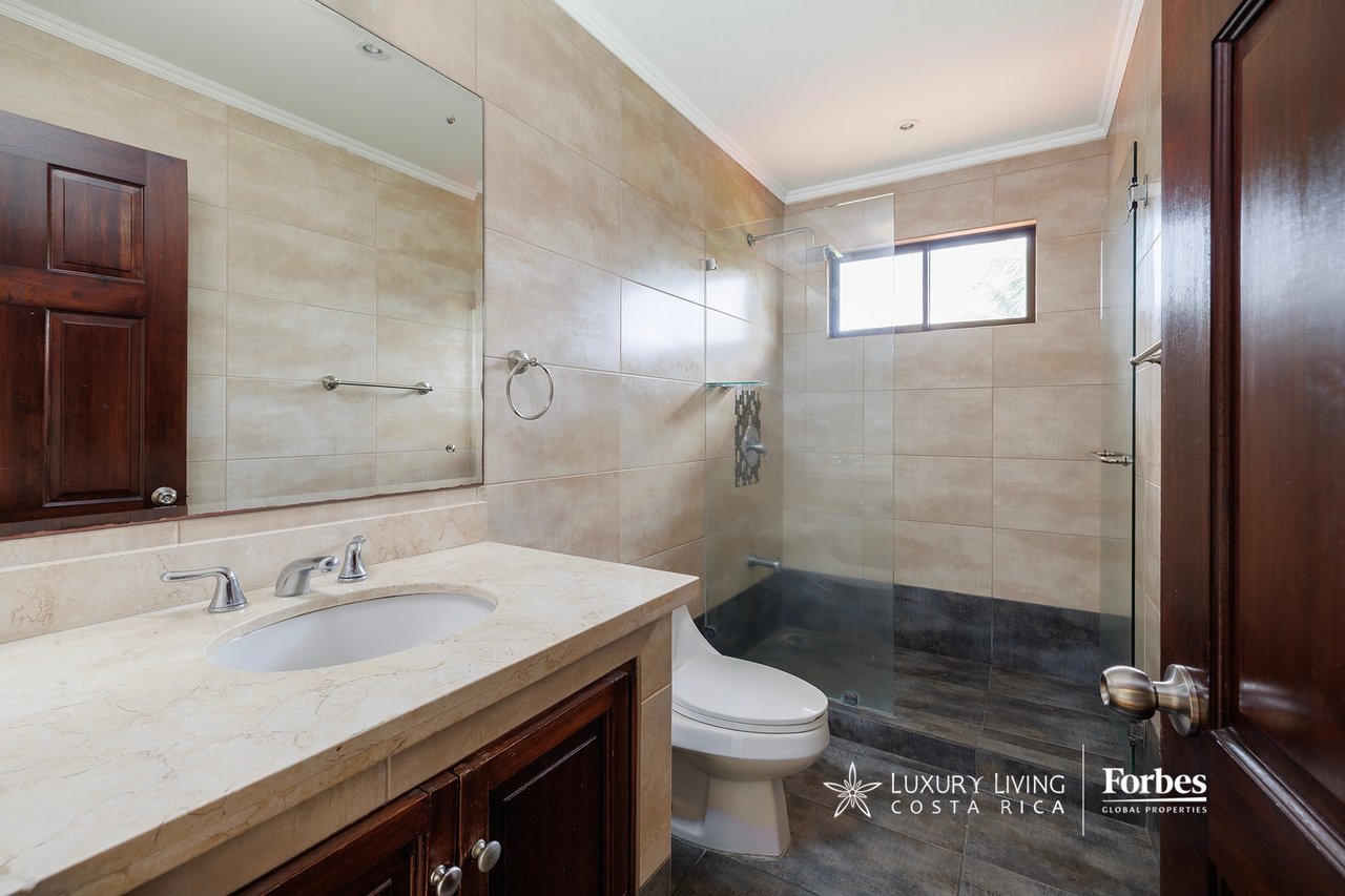 Bathroom with a glass shower, beige tile, dark flooring, and a wide stone vanity.