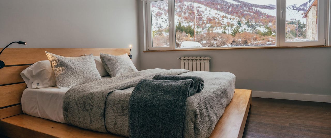 Bedroom with gray bedding and a wide window overlooking snow-dusted mountains.