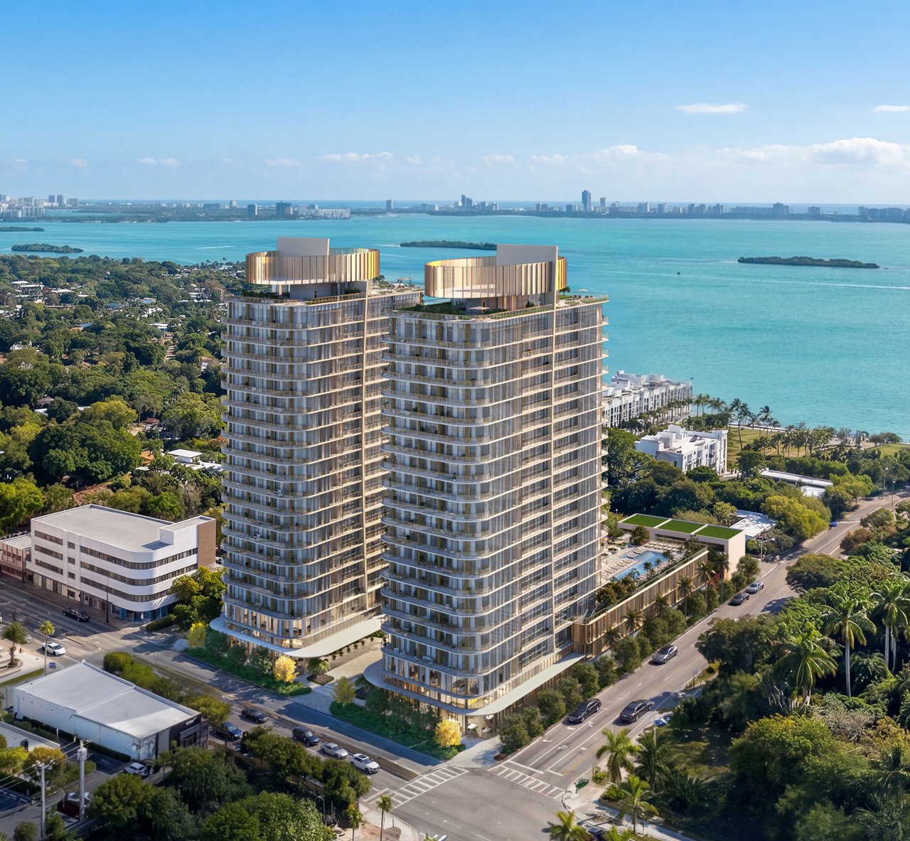 Kempinski Residences twin glass towers beside turquoise bay water, with a distant city skyline.