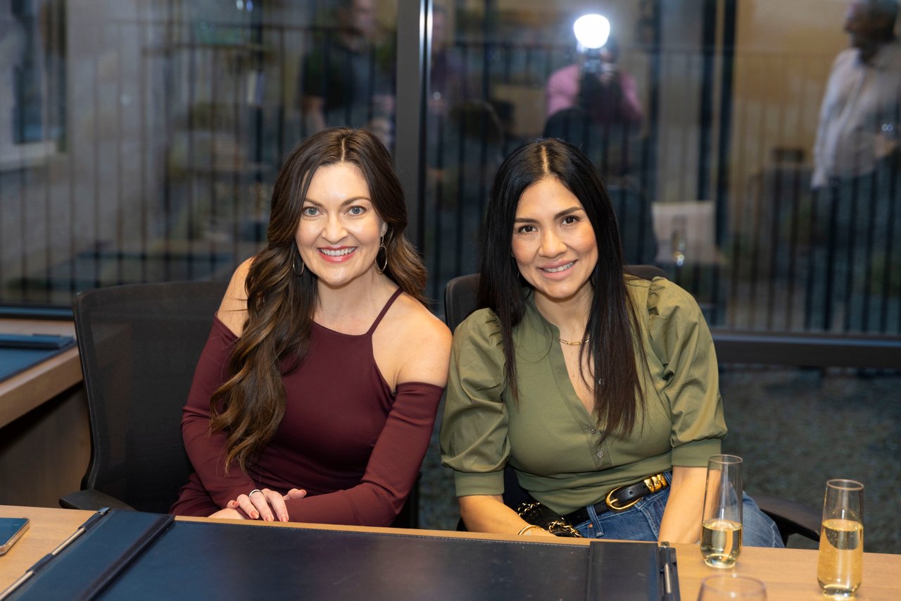 Two women seated together at an event table with champagne glasses.