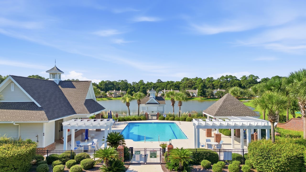Community pool beside a lake, with shaded pergolas and landscaped grounds.