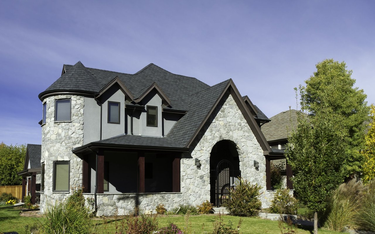 Two-story stone home with a rounded turret, steep dark roof, and arched front entrance.