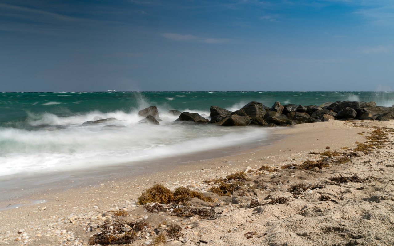 Sandy beach with turquoise surf breaking against a rocky shoreline.