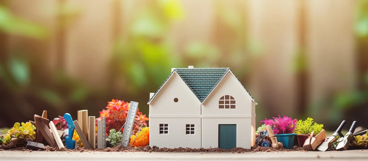 A miniature white house surrounded by gardening tools, plants, and building supplies.