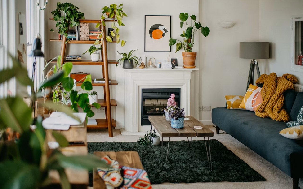 Furnished living room with a white fireplace, dark sofa, wooden coffee table, and leafy plants.