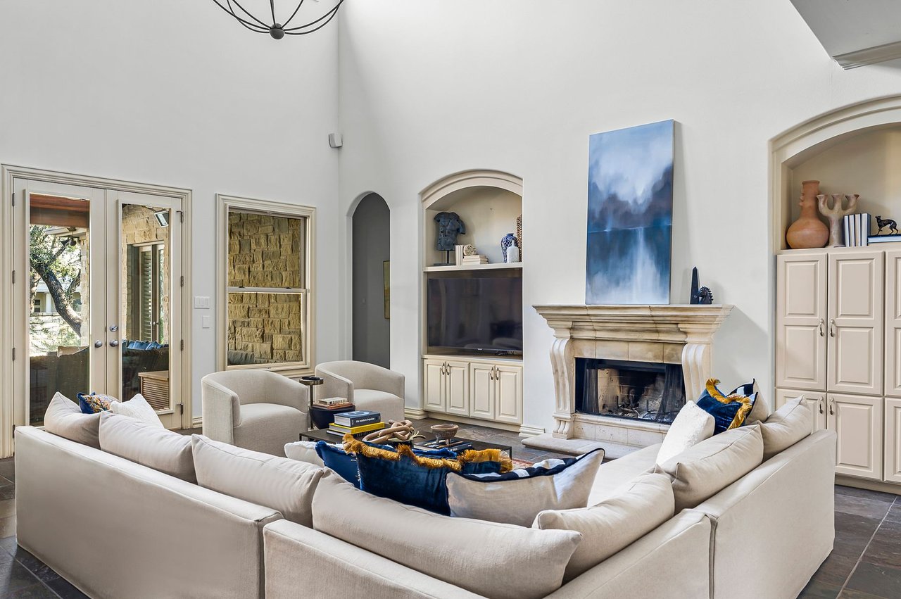 Living room with stone fireplace, mounted television, and French doors to the patio at 5902 Saratoga Cove, Davenport Ranch, Austin, Texas.