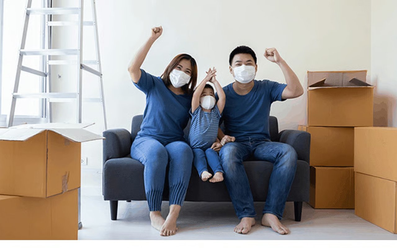 Masked family celebrates on a sofa among moving boxes.