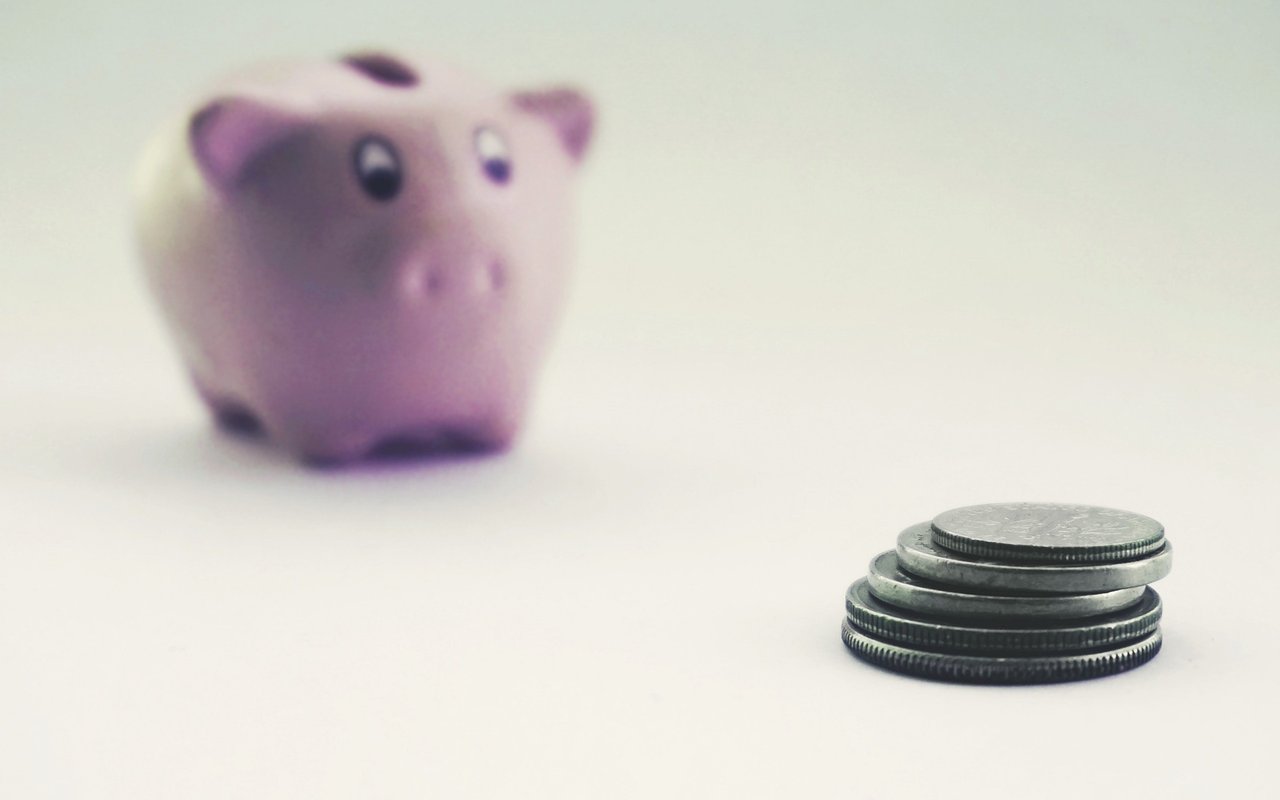 A stack of coins in front of a softly blurred pink piggy bank.