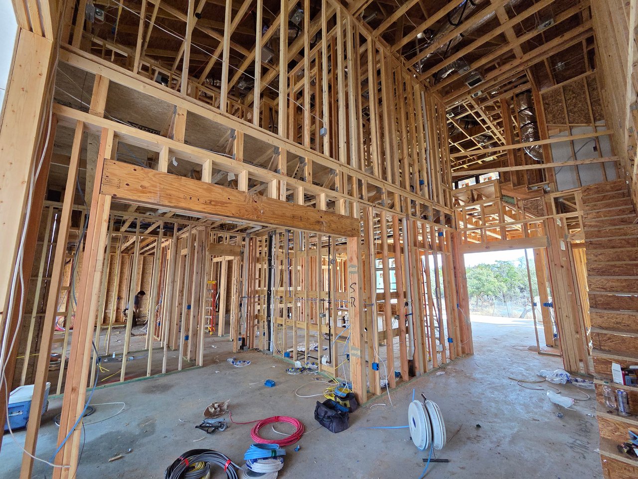 Unfinished home interior with exposed timber framing, tall ceilings, and electrical supplies on the floor.