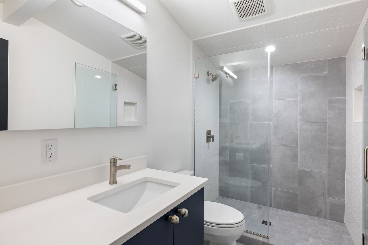 Bathroom with navy vanity, white sink, and glass shower tiled in gray.