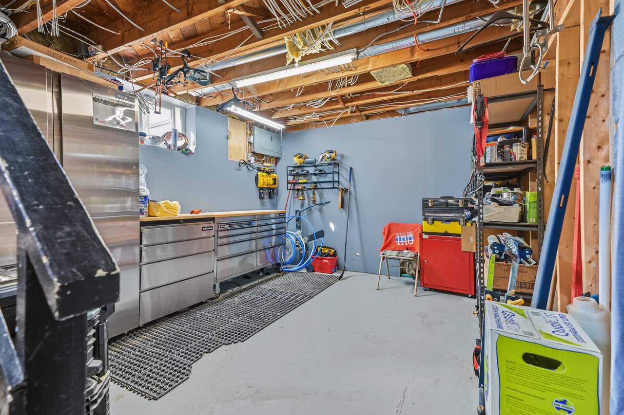 Basement workshop with stainless steel cabinets, wall-mounted tools, and a red tool chest.