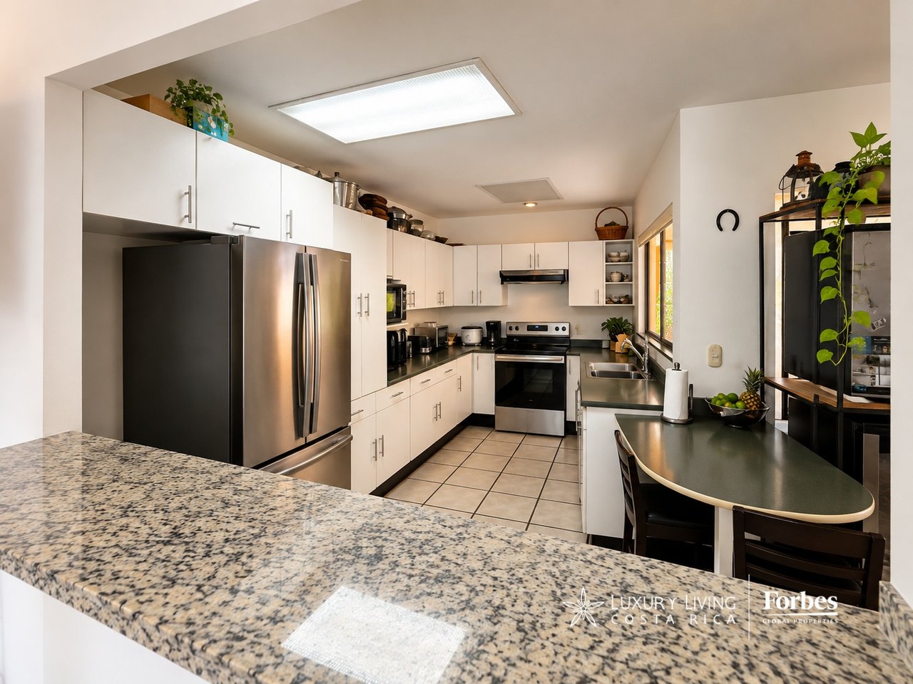 Kitchen with white cabinets, stainless-steel appliances, a double sink, and a large speckled stone island.