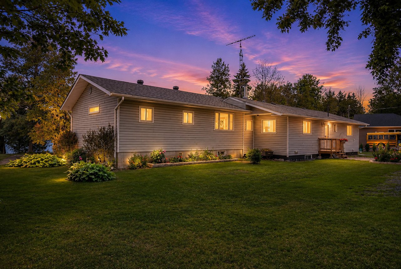 Single-story home with glowing windows, landscaped garden, and broad lawn at dusk.