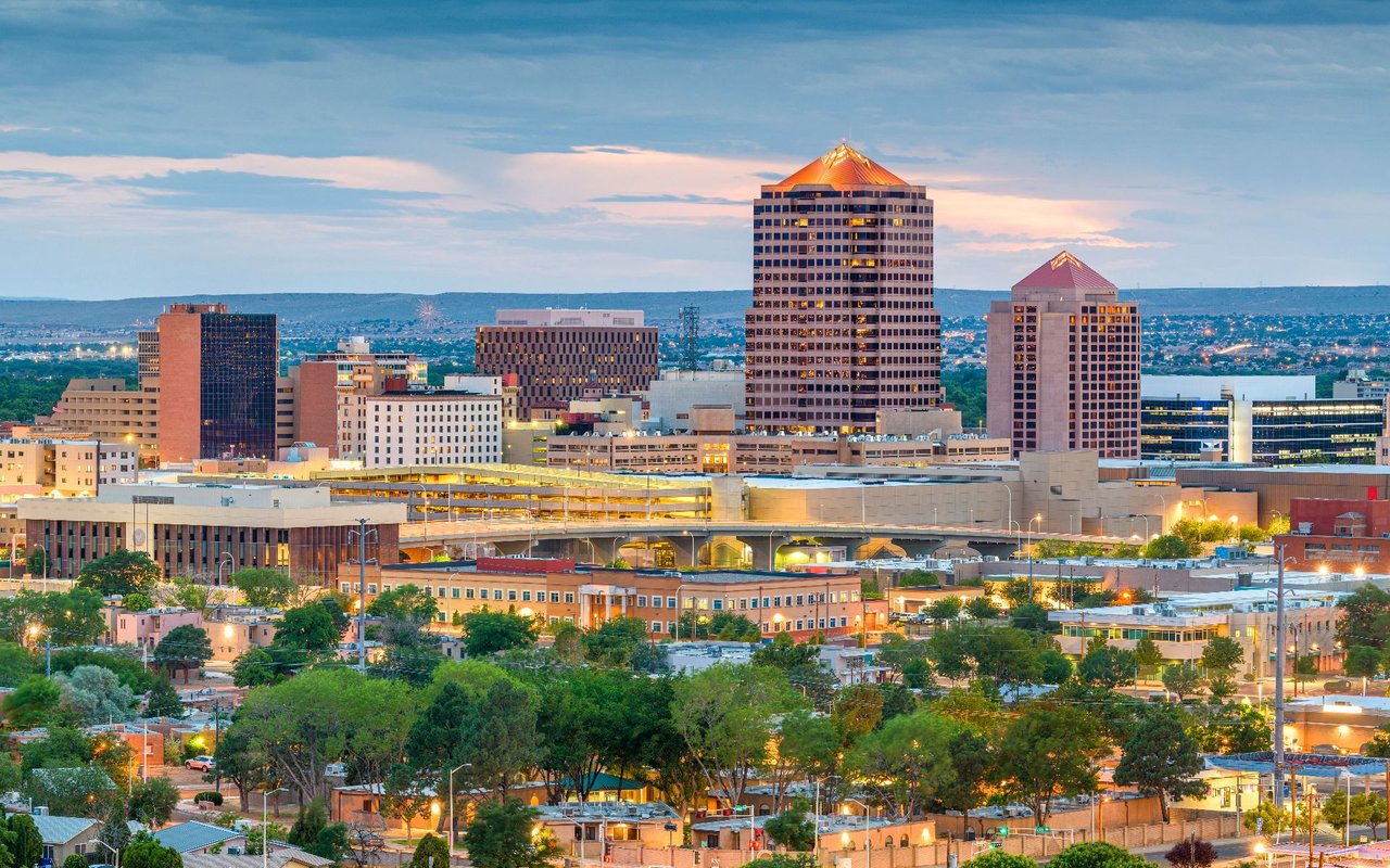Downtown Albuquerque at dusk, with illuminated towers and low-rise buildings.