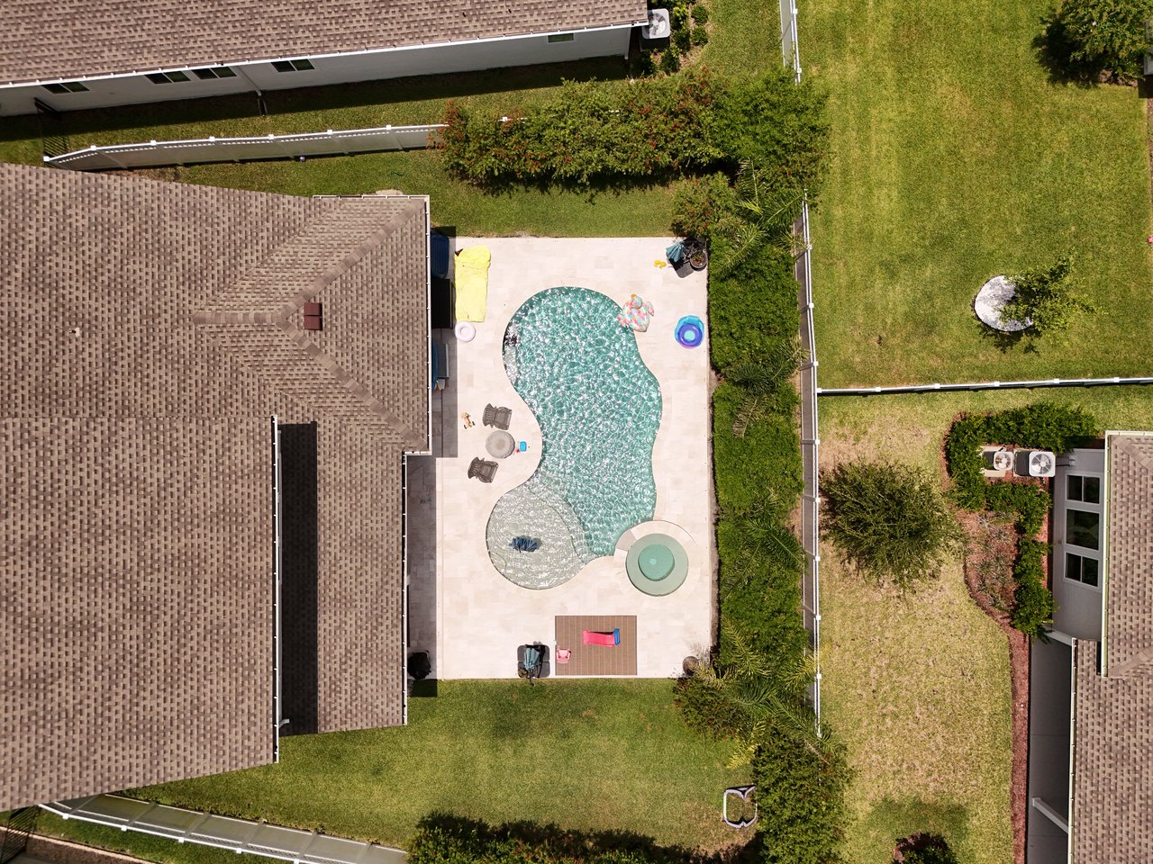 Aerial view of a backyard pool and patio between neighboring homes.