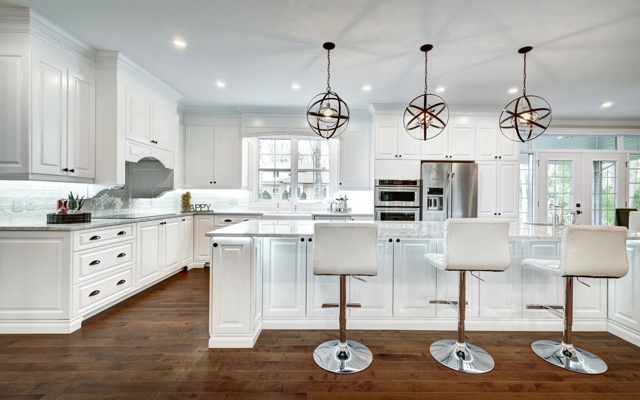 Bright white kitchen with a large marble island, three bar stools, and geometric pendant lights.
