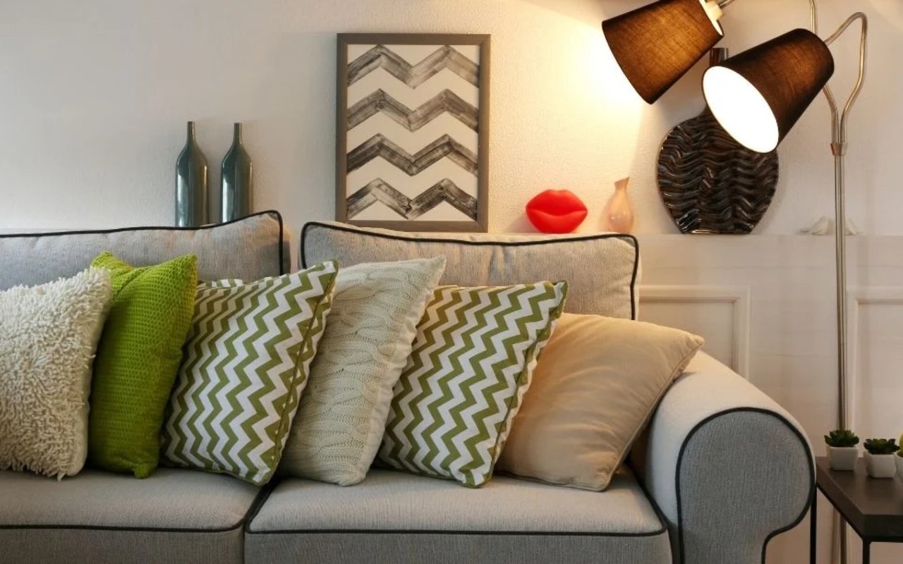 Gray sofa with green patterned pillows beside a two-shade floor lamp casting warm light.