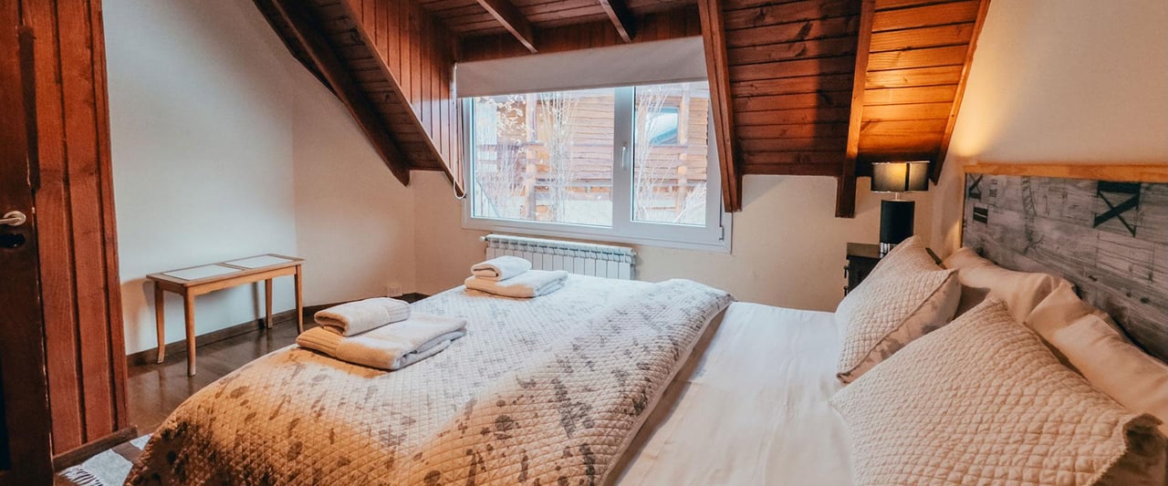 Attic bedroom with a double bed, folded towels, and exposed wood-beam ceiling.