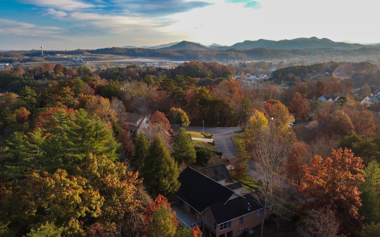 Aerial view of an autumn neighborhood, winding road, and distant mountain ridges.
