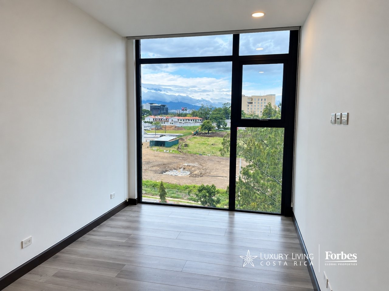 Empty apartment room with gray plank flooring and a large window overlooking distant mountains.
