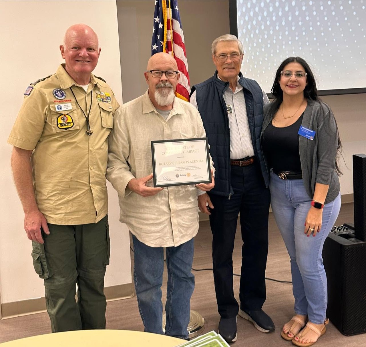 Four adults pose with a Rotary Club of Placentia certificate beside an American flag.
