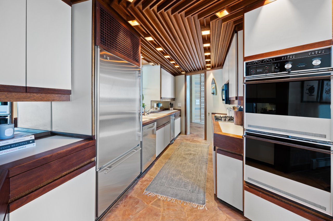 Galley kitchen with stainless-steel appliances, white cabinets, and a slatted wood ceiling.