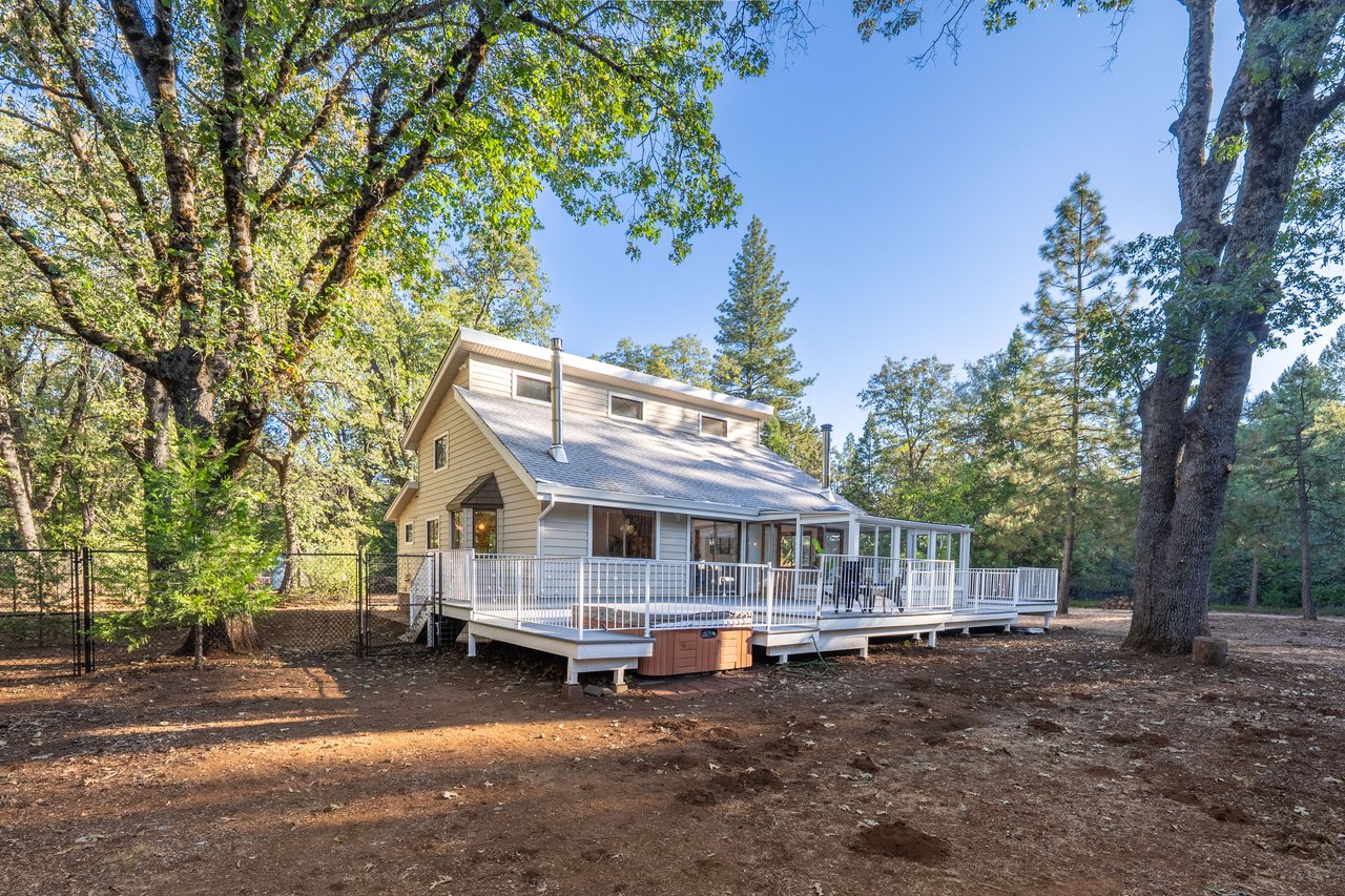 Two-story home with a broad white-railed deck and screened porch among mature trees.