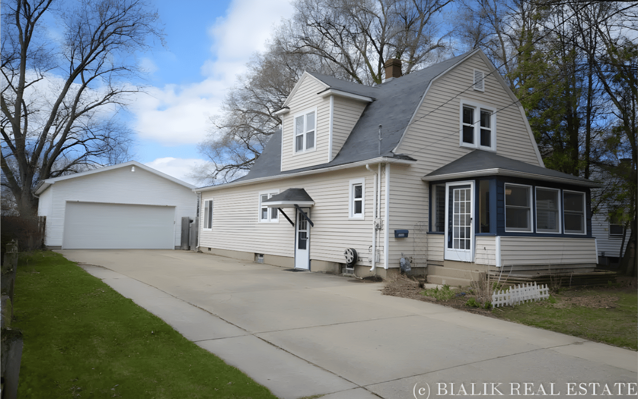 Light-colored two-story house with an enclosed porch, detached garage, and wide concrete driveway.