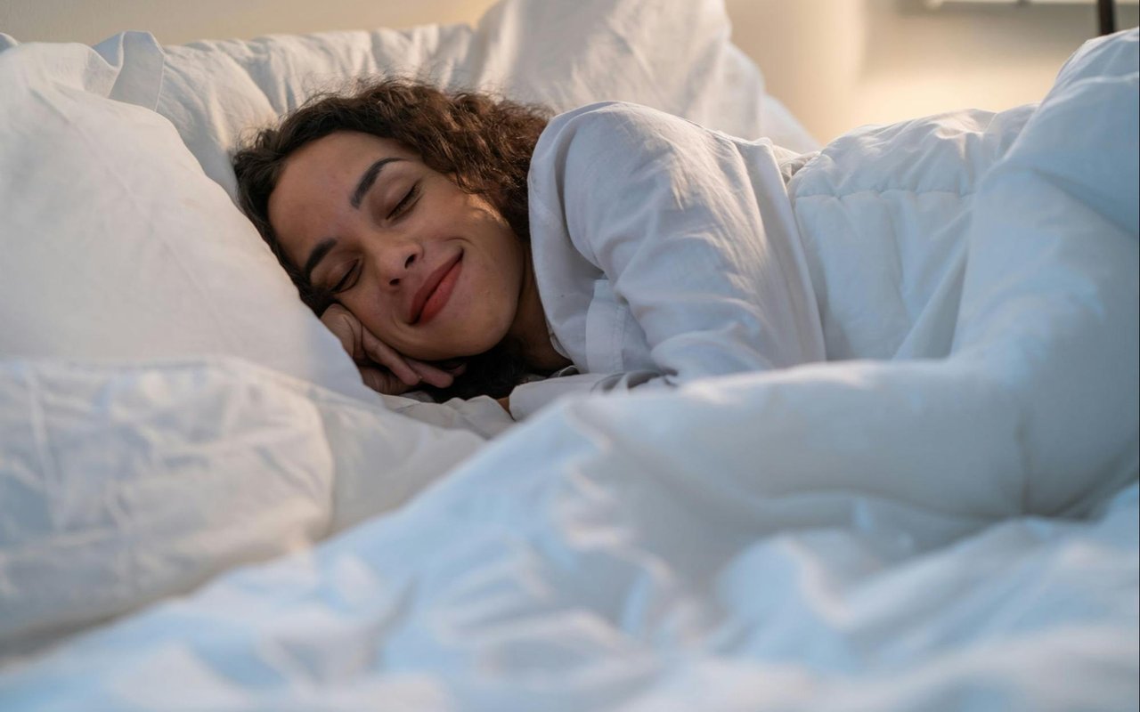 Woman sleeping peacefully on her side among white pillows and bedding.