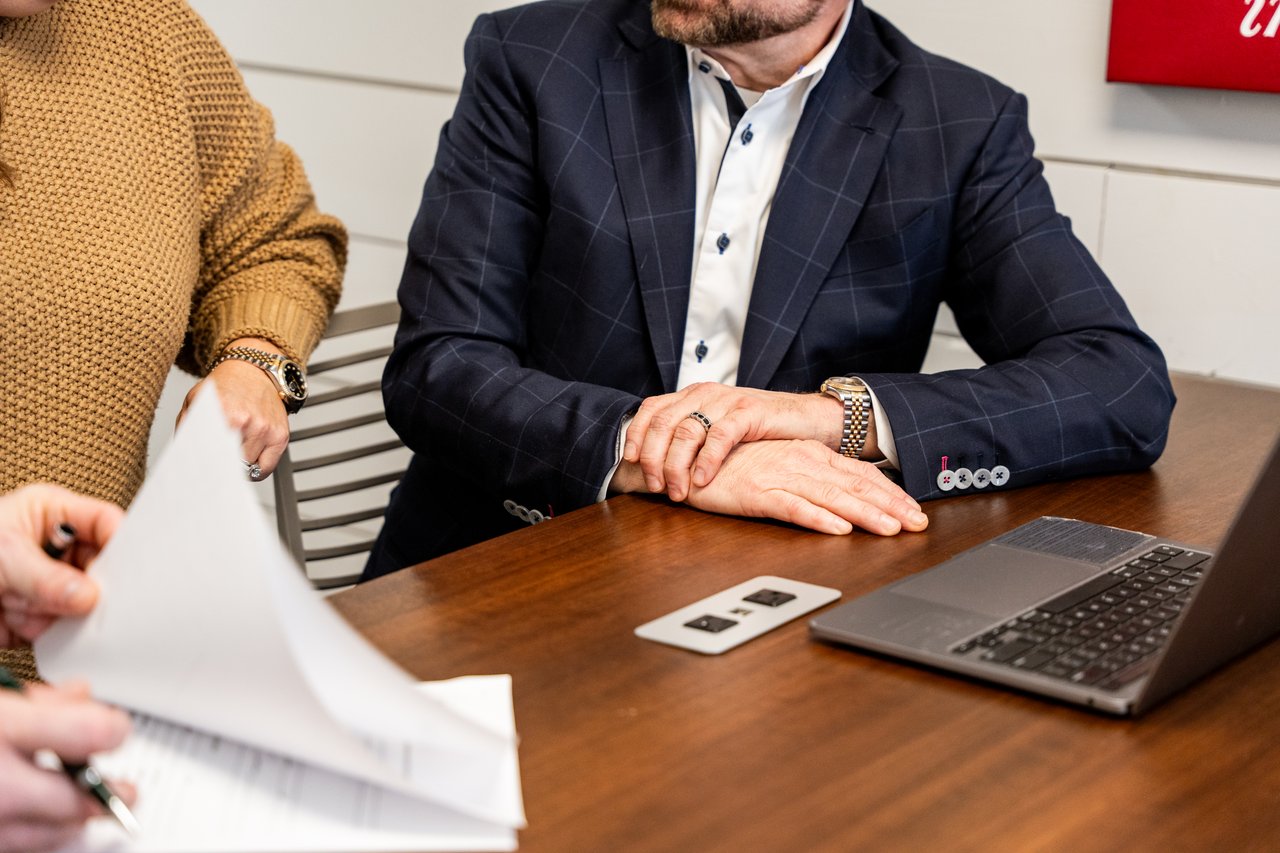 Two people review paperwork at a table beside an open laptop.