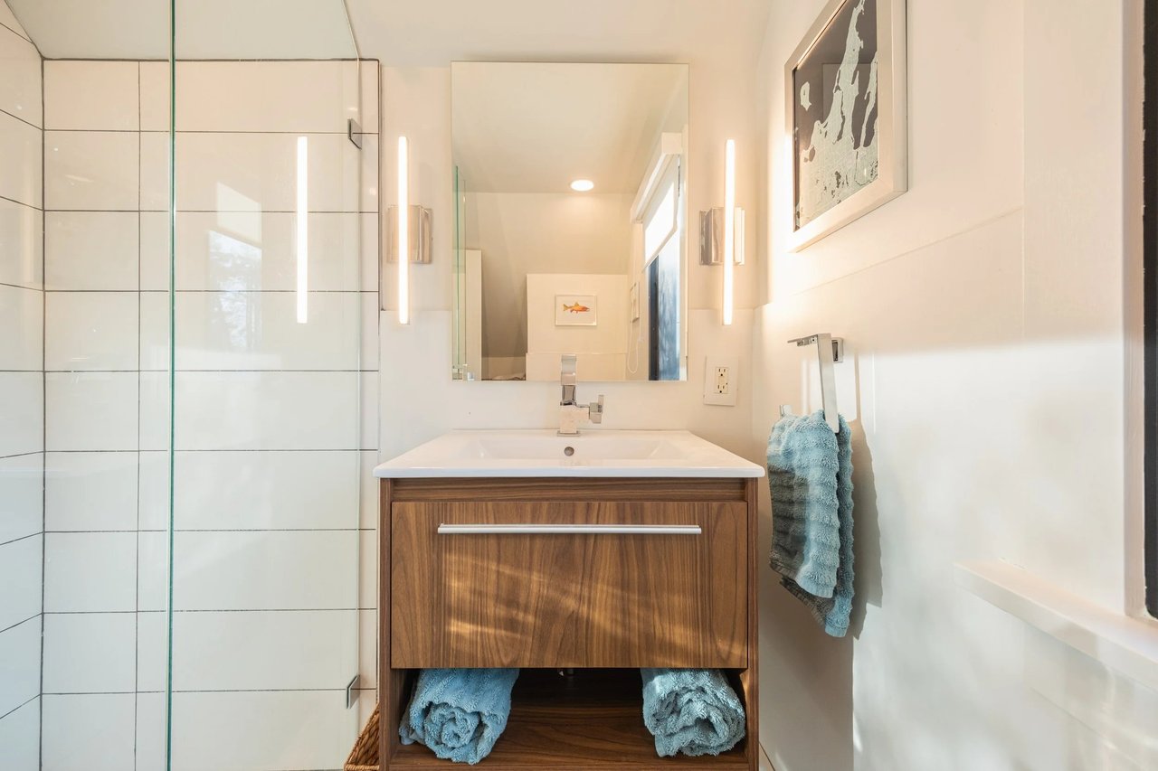 Renovated bathroom with a glass shower, white tile, and a wood vanity with blue towels.