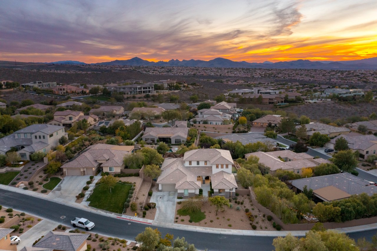 Aerial view of two-story homes and tree-lined streets in Anthem Country Club, Henderson, Nevada at sunset, with desert foothills and mountains on the horizon