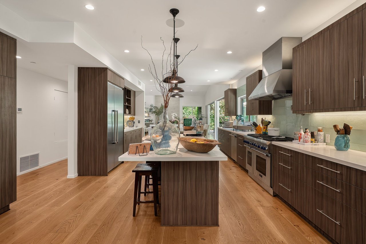 Modern kitchen with dark wood cabinetry, a large island, stainless appliances, and an open living area beyond.