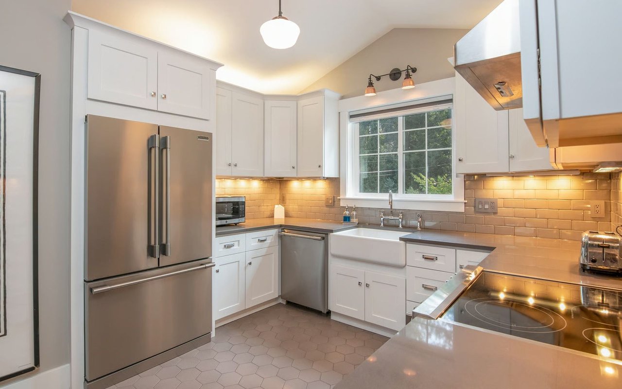 Bright white kitchen with stainless-steel appliances, farmhouse sink, and large window.