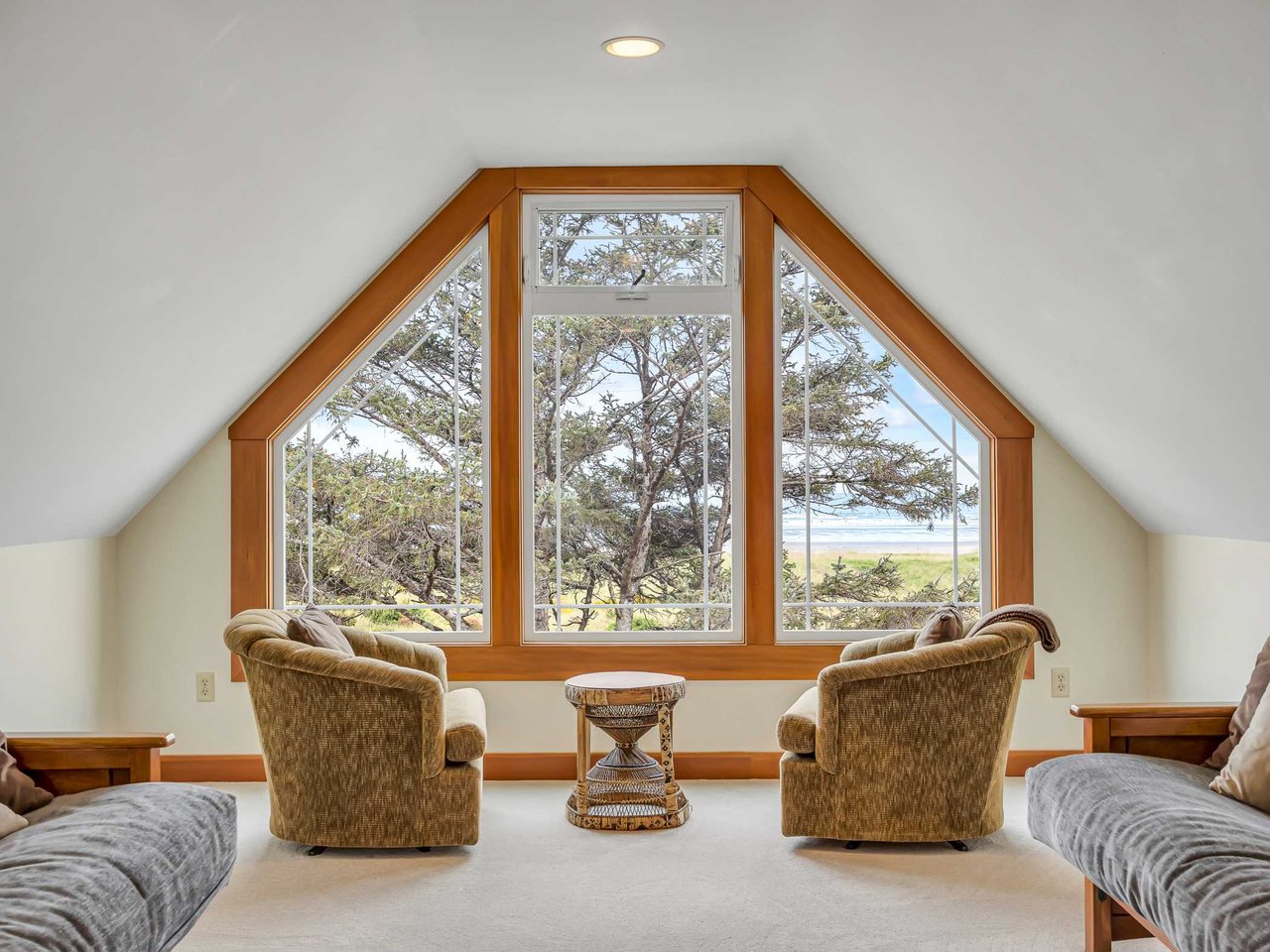 Inviting upper-level retreat featuring a vaulted ceiling, expansive custom window, comfortable seating area, and serene views of the Oregon Coast landscape
