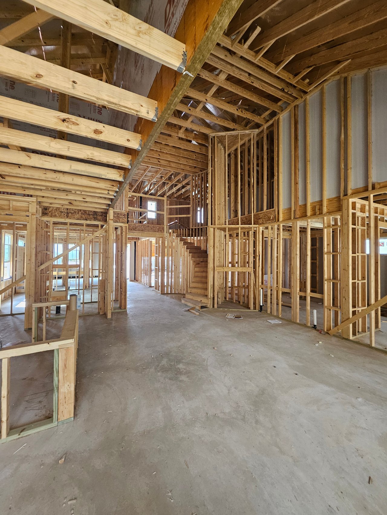 Unfinished home interior with exposed framing, vaulted ceiling, and central staircase.