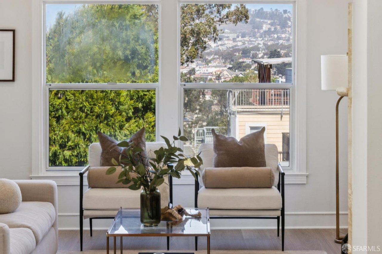 Living room with cream seating and large windows overlooking trees and a hillside cityscape.