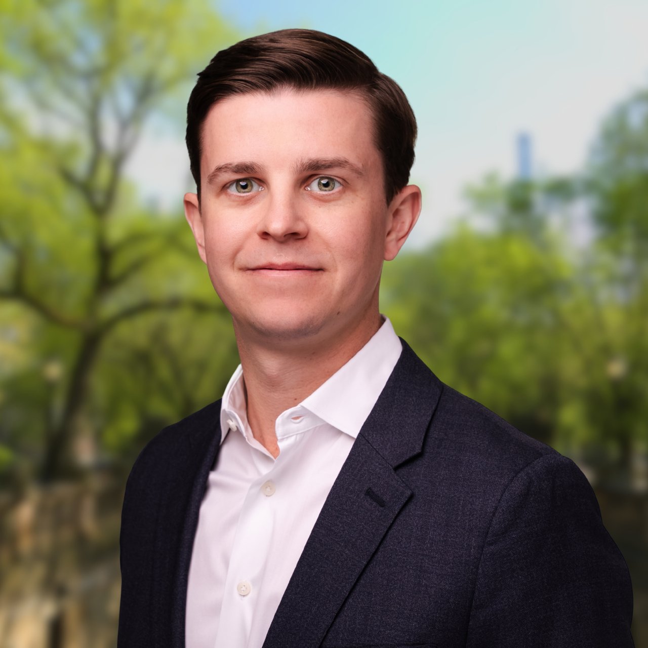 Brian Peer in a dark suit jacket and white shirt against a blurred leafy background.